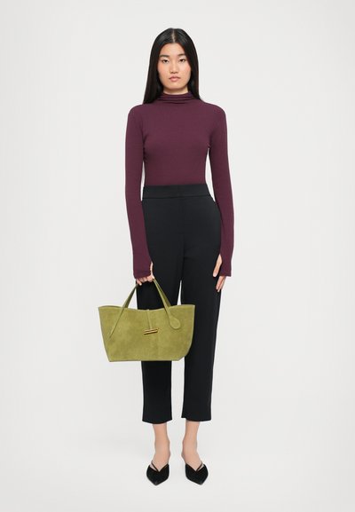 Geantă tote din suede verde măsliniu, cu mânere duale, având un accent auriu. Asortată cu un pulover cu guler înalt de culoare burgundă și pantaloni negri scurți.