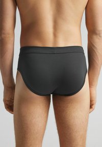 Zwarte zwemslips voor mannen met een gladde textuur, aansluitend ontwerp en een lage taille. Heeft minimale stiksels en zijopeningen.