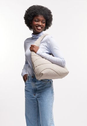 Borsa a spalla beige puffosa con texture trapuntata, forma morbida, indossata sopra un dolcevita azzurro chiaro, abbinata a jeans chiari a vita alta.