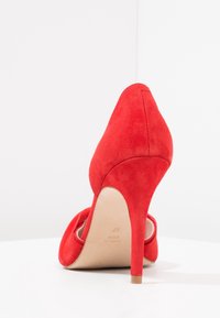 Chaussure à talon haut en suede rouge vue de l'arrière, montrant le talon et la semelle marquée "Fabriqué en Espagne, taille 37."