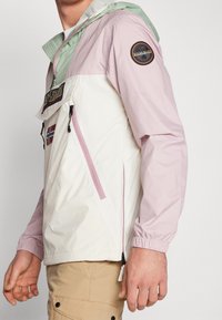 Lätt, färgblockerad jacka i vitt, rosa och grönt. Har elastiska muddar, fickor med dragkedja och en logotypapplikation på ärmen.