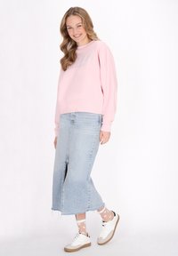 Felpa rosa chiaro con vestibilità oversize, gonna di jeans blu chiaro con spacco frontale, sneakers bianche e calzini alla caviglia con motivo.