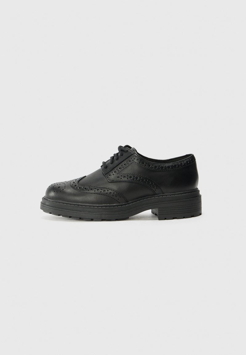Chaussure brogue en cuir noir avec perforations en forme d'ailes, design à lacets et semelle épaisse en caoutchouc, vue de profil sur un fond neutre.