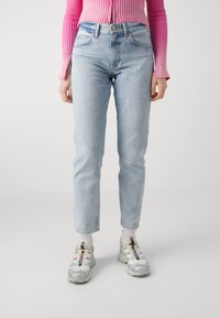 Jeans de mezclilla azul claro con corte recto y cinco bolsillos, combinados con zapatillas deportivas multicolor y calcetines blancos.