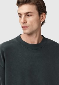 Felpa grigia scura con colletto rotondo a costine, texture morbida e vestibilità rilassata, caratterizzata da sottili dettagli di cucitura e senza motivi visibili.