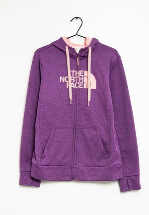 Fioletowa bluza z kapturem na zamek, z różowymi sznurkami, przednimi kieszeniami oraz logo "The North Face" w jasnoróżowym kolorze na piersi, zawieszona na czarnym wieszaku.