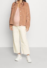 Veste en velours côtelé rose poudré, boutonnée, avec deux poches avant. Portée sur un pull rose et associée à un pantalon large crème et des baskets blanches.