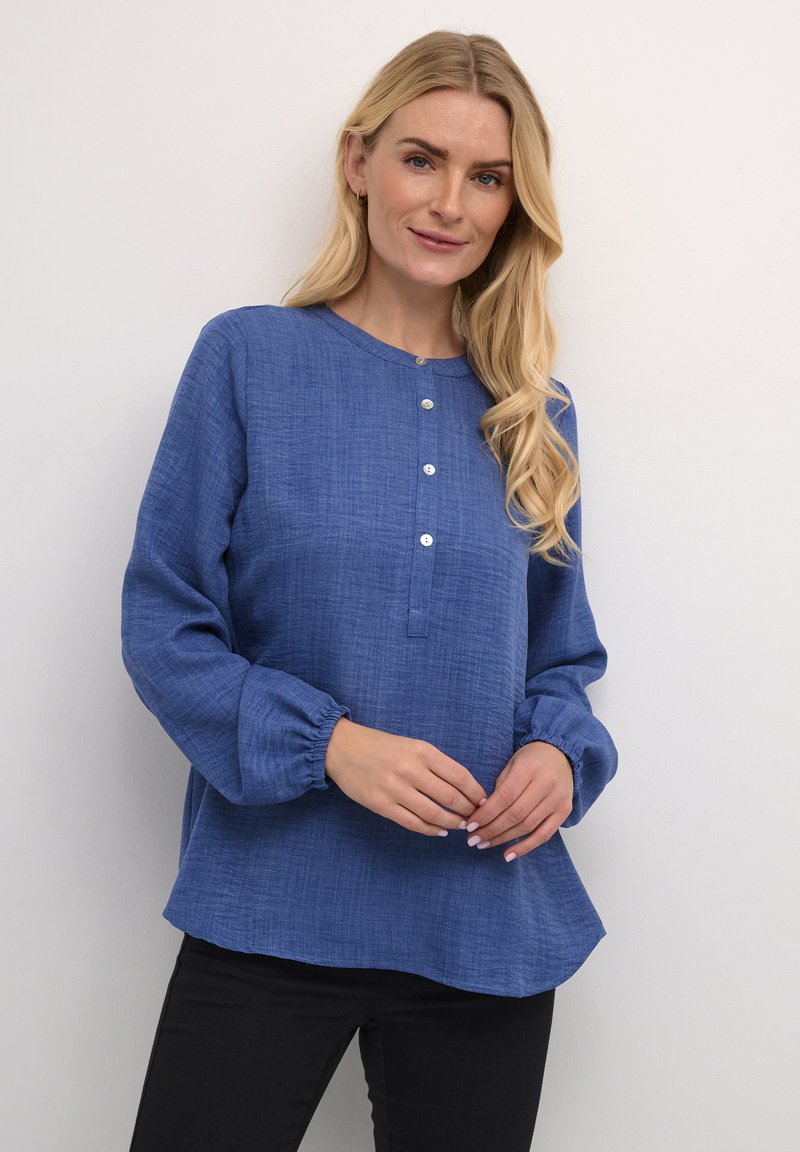 Blauwe blouse met lange mouwen, ronde halslijn, knoopsluiting en gathered manchetten. Gemaakt van een textuurstof, met een licht ontspannen pasvorm.
