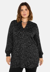 Černá tunika s šedým zvířecím vzorem, s výstřihem do V, dlouhými nafouklými rukávy s elastickými manžetami a volným střihem. Měkká, texturovaná tkanina.