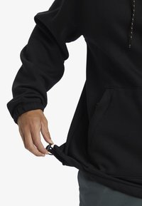 Černá mikina s kapucí má stahovací šňůrku, přední klokaní kapsu, elastické manžety a zip na lemu, což ukazuje na ležérní strukturovanou tkaninu.