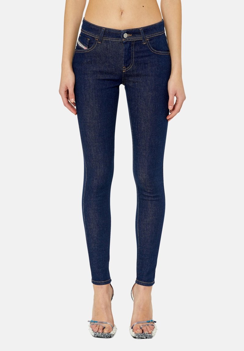 Jeans skinny de un azul oscuro, confeccionados en denim, con un diseño clásico de cinco bolsillos y detalles de costura sutiles. Llevados con tacones delgados.