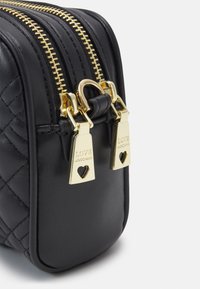 Černý prošívaný kožený roh tašky se dvěma zlatými zipy, každý s obdélníkovým jezdcem s rytím "LOVE MOSCHINO" a výřezem ve tvaru srdce.