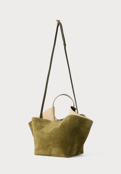 Sac fourre-tout en suède vert avec un haut beige contrastant, présentant un design décontracté, une longue sangle d'épaule réglable et de courtes poignées.