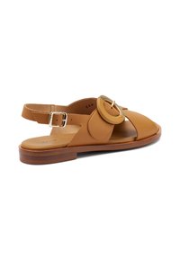 Sandalo in pelle marrone chiaro con punta arrotondata, cinturini larghi e un accento circolare. Presenta un basso tacco in legno e una cinghia alla caviglia regolabile.