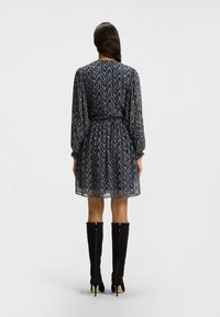 Abito a fantasia navy con maniche lunghe, vita stretta e gonna ampia, abbinato a stivali neri al ginocchio. Materiale traslucido.