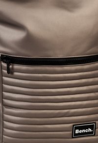Grijze rugzak van glad materiaal, met een ribbelontwerp op de onderste helft, een zwart ritsvak en een zwart logo-label.