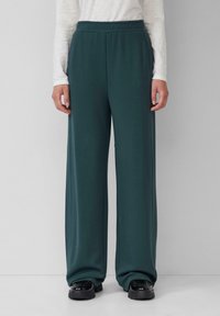 Pantalons larges teal avec une taille élastique, fabriqués à partir d'un tissu doux. Pas de motifs ou d'éléments visibles. Associés à des chaussures noires épaisses.