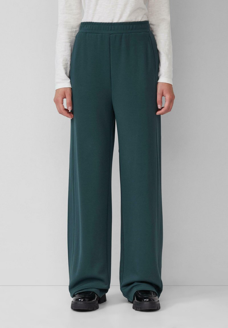 Pantalons larges teal avec une taille élastique, fabriqués à partir d'un tissu doux. Pas de motifs ou d'éléments visibles. Associés à des chaussures noires épaisses.