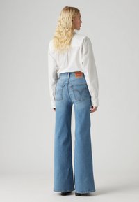 Kék, magas derekú, trapézszárú farmernadrág. Hátsó részén bőr címkét visel logóval, két hátsózsebbel és hímzett mintával.