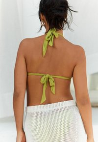 Groene geribde halter bikini top die om de nek is vastgebonden, gecombineerd met een witte gebreide rok met een open maasontwerp.