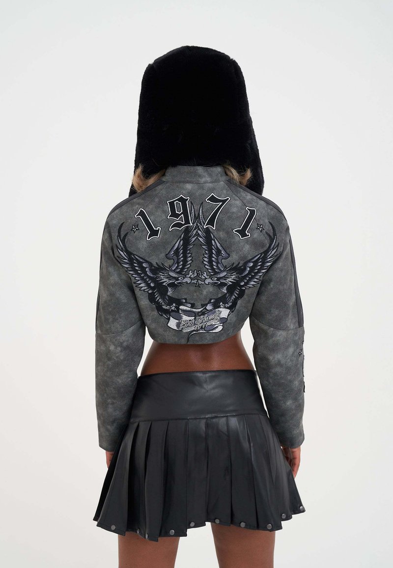 Gray suede bomber jacket with an eagle design and '1971' lettering on the back, paired with a pleated black leather mini skirt.