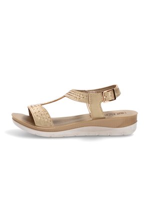 Sandalia beige de mujer con diseño de tira en T, pequeños tachones decorativos, correa con hebilla ajustable, suela acolchada y suela blanca texturizada.