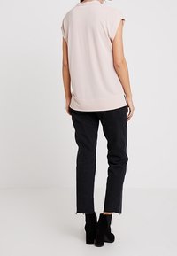 Ljust rosa ärmlös topp med en avslappnad passform, kombinerad med svarta smala jeans och ankelboots. Toppen har en rundad halsringning.