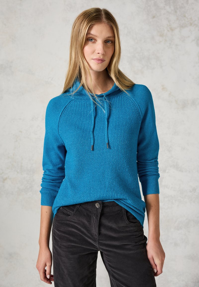 Sweat à capuche bleu avec texture côtelée, manches longues et cordon de serrage. Associé à un pantalon en velours côtelé noir avec poches latérales.
