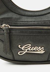 Borsa a tracolla in faux leather nera con un design arrotondato, tasca con zip e un accento del logo "Guess" in tonalità oro sul davanti.