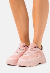 Ljust rosa träningsskor med en blandning av släta och texturerade material, vadderad krage och snörning, med en tjock yttersula.