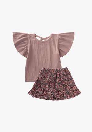 Kratki rukavi, prašnjavo ružičasti rebrasti top s širim rukavima i detaljem leđa u obliku križa, uparen s tamnom suknjom s cvjetnim uzorkom i volanima.