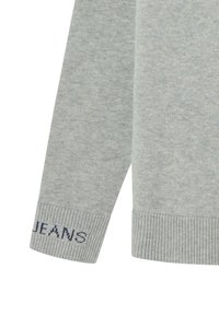 Suéter de punto gris con puños de canalé, con "JEANS" tejido en azul oscuro en la parte inferior de la manga. Textura suave, cuello redondo clásico.