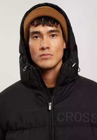 Czarna kurtka puchowa z zapięciem na zamek, dużym kapturem i wytłoczonym logo. W komplecie z brązową dzianinową czapką, która zwiększa ciepło.