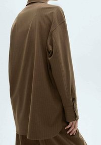 Chemise brune à rayures avec des manches longues et un col classique. Comprend des poignets boutonnés et une coupe décontractée. Tissu lisse et texturé.