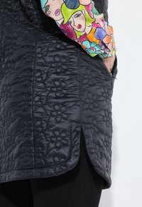 Svart quiltrad kjol med blommönster, bärs tillsammans med en färgglad långärmad skjorta prydd med abstrakt illustrerade ansikten och blommor.