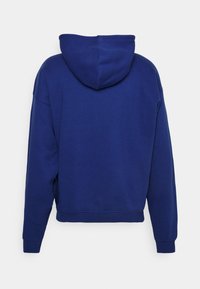 Felpa blu con tasca a marsupio frontale, vestibilità oversize e materiale in cotone testurizzato. Presenta una cappuccio con cordino e polsini a coste.