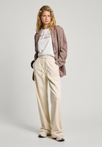 Blazer de cuadros en marrón y beige, camiseta gráfica blanca, pantalones crema con cordón, y calzado beige. Texturas suaves y ajuste relajado.