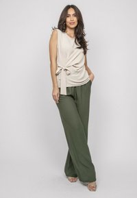Débardeur beige sans manches avec un détail de nœud à l'avant et un pantalon large vert. La tenue a une coupe décontractée, fabriquée dans un tissu léger.