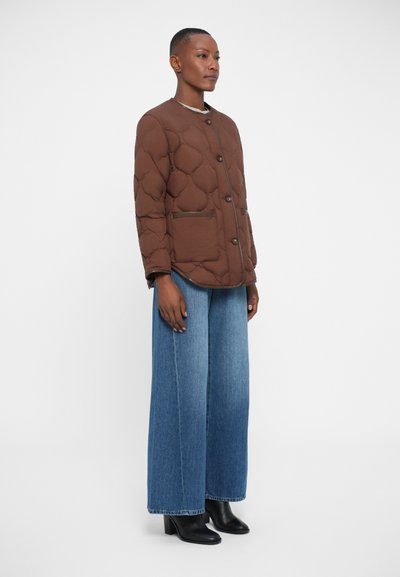 Giacca trapuntata marrone con collo rotondo, chiusura con bottoni e tasche laterali, abbinata a jeans in denim blu a gamba larga e stivaletti neri.