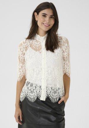 Bluză din dantelă în alb-off cu mâneci scurte, guler înalt și închidere cu nasturi. Prezintă modele florale intricate și un tiv ondulat.
