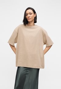 T-shirt ample marron clair en coton doux avec manches courtes et encolure ronde, associé à une jupe midi verte en satin.