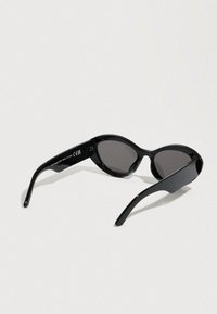 Lunettes de soleil ovales noires avec des verres foncés, monture en plastique élégante et branches courbées. Détail de surface texturée sur les branches.