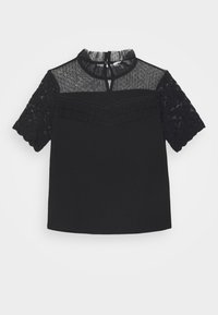 Blouse noire à manches courtes avec manches en dentelle, encolure transparente à pois, bordure à volants sur la poitrine et petite fermeture bouton en forme de trou à la nuque.