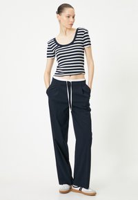 Stribet kortærmet top i navy og hvid, parret med navy brede bukser med snoretræk i taljen. Fodtøj: hvide sneakers med lysebrune såler.