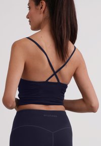 Top sportivo blu navy con spalline incrociate e dettaglio arricciato sulla schiena, realizzato in un materiale morbido ed elastico.