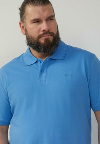 Lichtblauwe poloshirt van gestructureerde stof. Voorzien van een klassieke kraag, twee knopen en een klein logo op de borst.