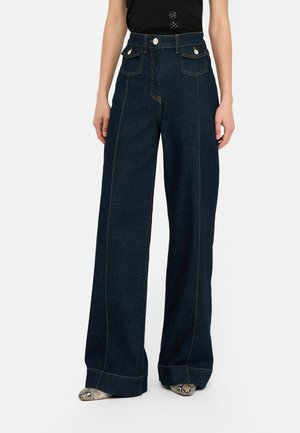 Pantalones de mezclilla de pierna ancha en azul oscuro con costuras en contraste y bolsillos frontales. Con características de cintura alta y cierres de botón metálico.