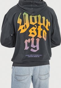 Sort hættetrøje med oversize pasform. Har flerfarvet grafik "Your Story" på ryggen med tekst under. Bomuldsstof, afslappet design.