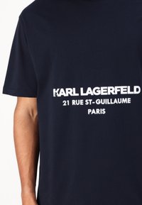 Granatowa bawełniana koszulka z wyróżniającym się białym napisem: „KARL LAGERFELD 21 RUE ST-GUILLAUME PARYŻ.” Okładka okrągła i krótkie rękawy.