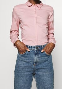 Ljusrosa, knapp-up skjorta med krage, gjord av slät tyg, tillsammans med högmidjade denimjeans med en klassisk blå tvätt.